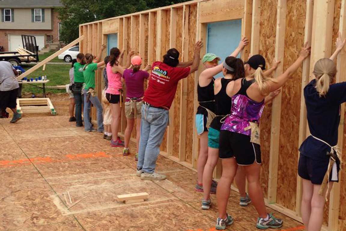 line of people hold walls up to construct a house